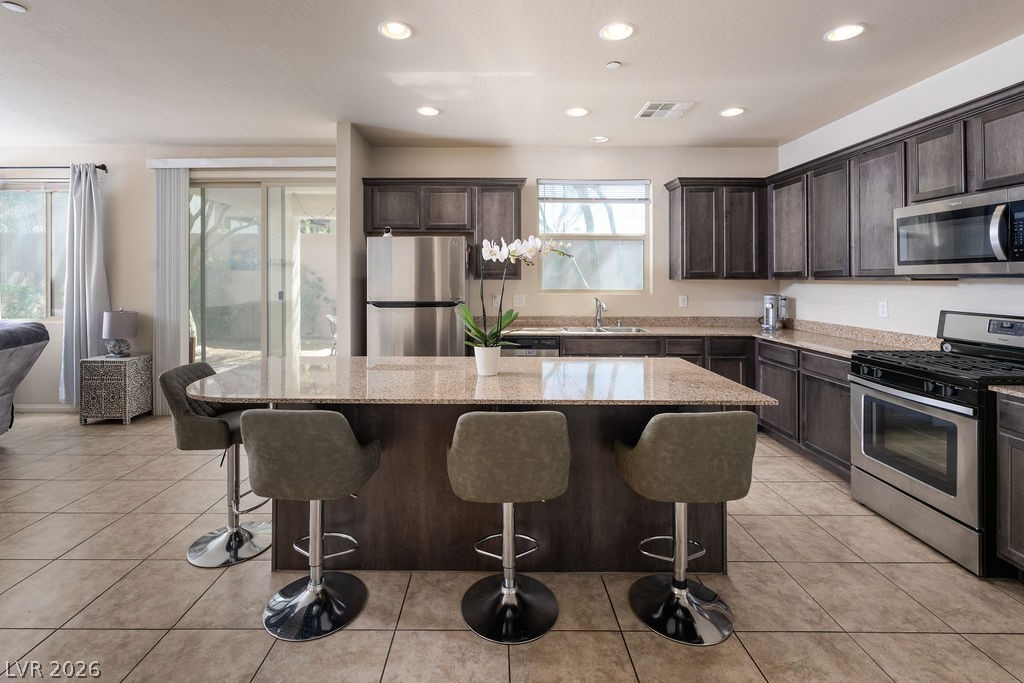 3069 Scenic Rhyme Avenue Henderson, NV 89044 - Photo 4 of 29 The heart of the home in one frame: granite island with bar seating for four, dark wood cabinetry, stainless appliances, and a living room that flows straight to the covered patio through a full-width sliding door. No walls between where the family cooks, eats, and relaxes.