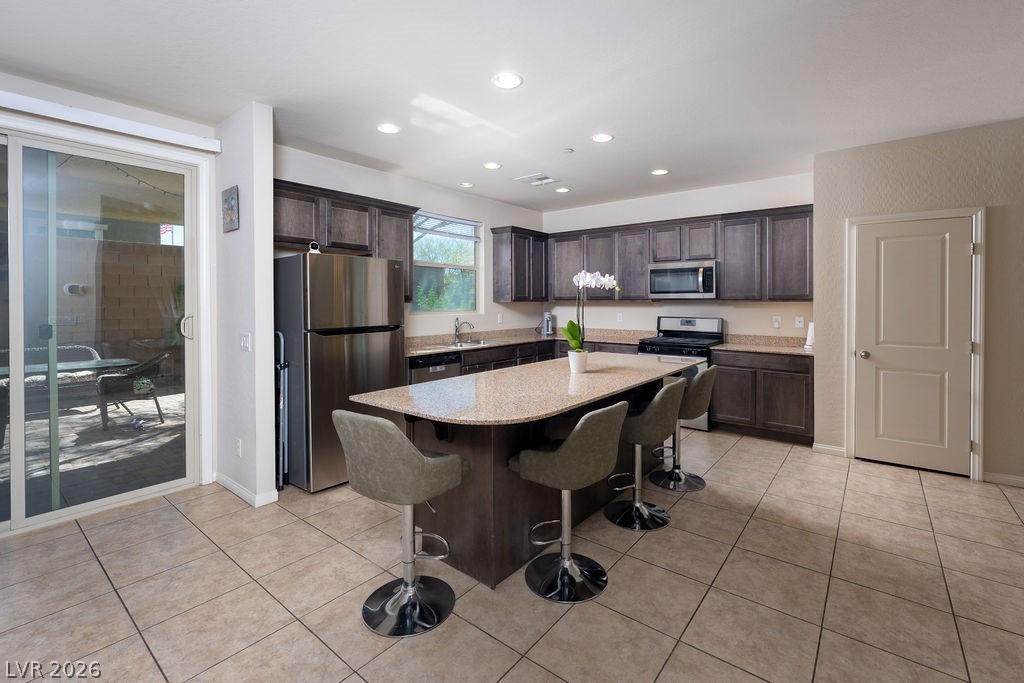 3069 Scenic Rhyme Avenue Henderson, NV 89044 - Photo 5 of 29 Oversized granite island with seating, a full run of dark cabinetry with crown detail, and a complete stainless appliance suite — this is the kitchen that comes move-in ready. No updates needed; just move in and start cooking.