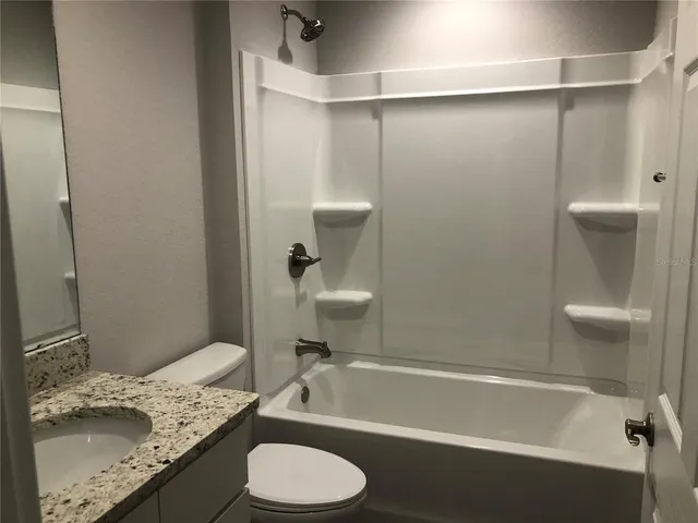 a bathroom with a granite countertop bathtub sink vanity mirror and toilet