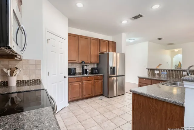 a kitchen with stainless steel appliances granite countertop a refrigerator a stove and a sink with wooden cabinets