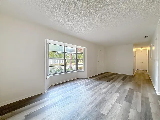 an empty room with wooden floor kitchen view and windows