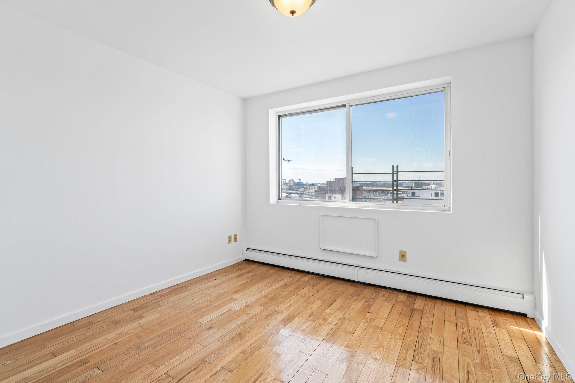 136-16 31st Road, Unit 8B Queens, NY 11354 - Photo 14 of 23 Empty room featuring light wood-type flooring and baseboard heating