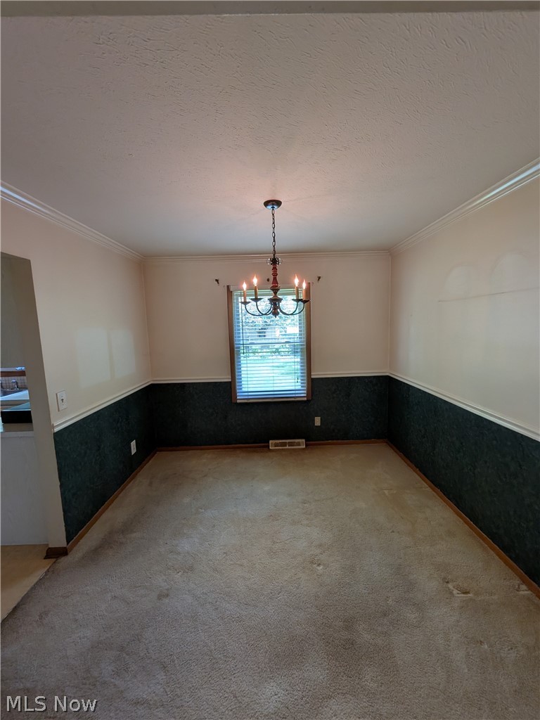 1161 Gulf Road Elyria, OH 44035 - Photo 10 of 34 Carpeted room featuring a window with blinds, a hanging chandelier, crown molding, and two-tone wall paneling
