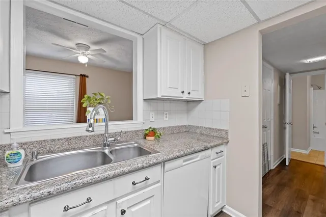 a kitchen with stainless steel appliances granite countertop a sink dishwasher and white cabinets with wooden floor