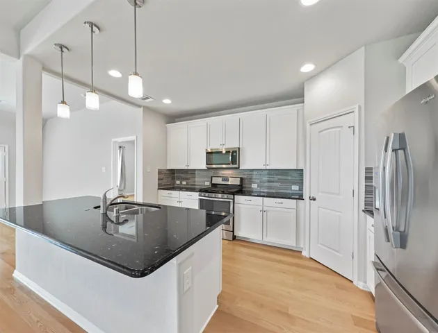 a kitchen with stainless steel appliances granite countertop a sink a stove a refrigerator and island with wooden floor