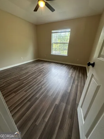 an empty room with wooden floor chandelier fan and windows