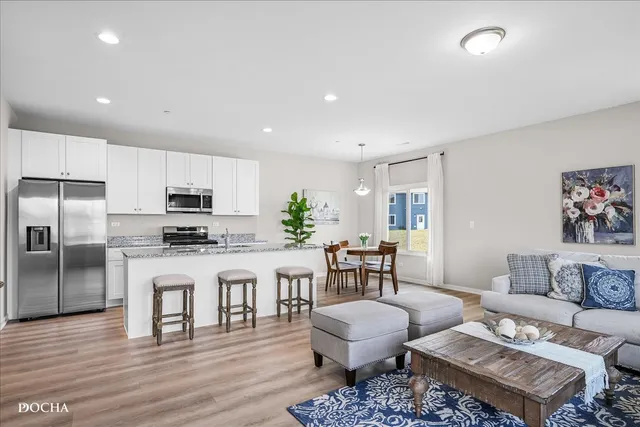 a living room with stainless steel appliances furniture a rug and a kitchen view