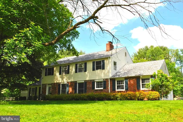 a view of a white house with a big yard and potted plants and large trees