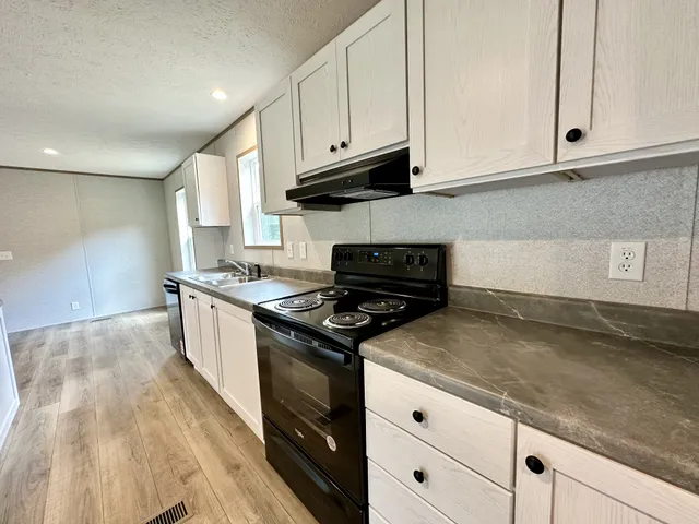 a kitchen with granite countertop a stove a sink and dishwasher wooden cabinets