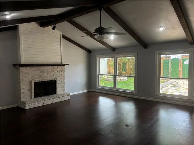 a view of an empty room with wooden floor fireplace and a window