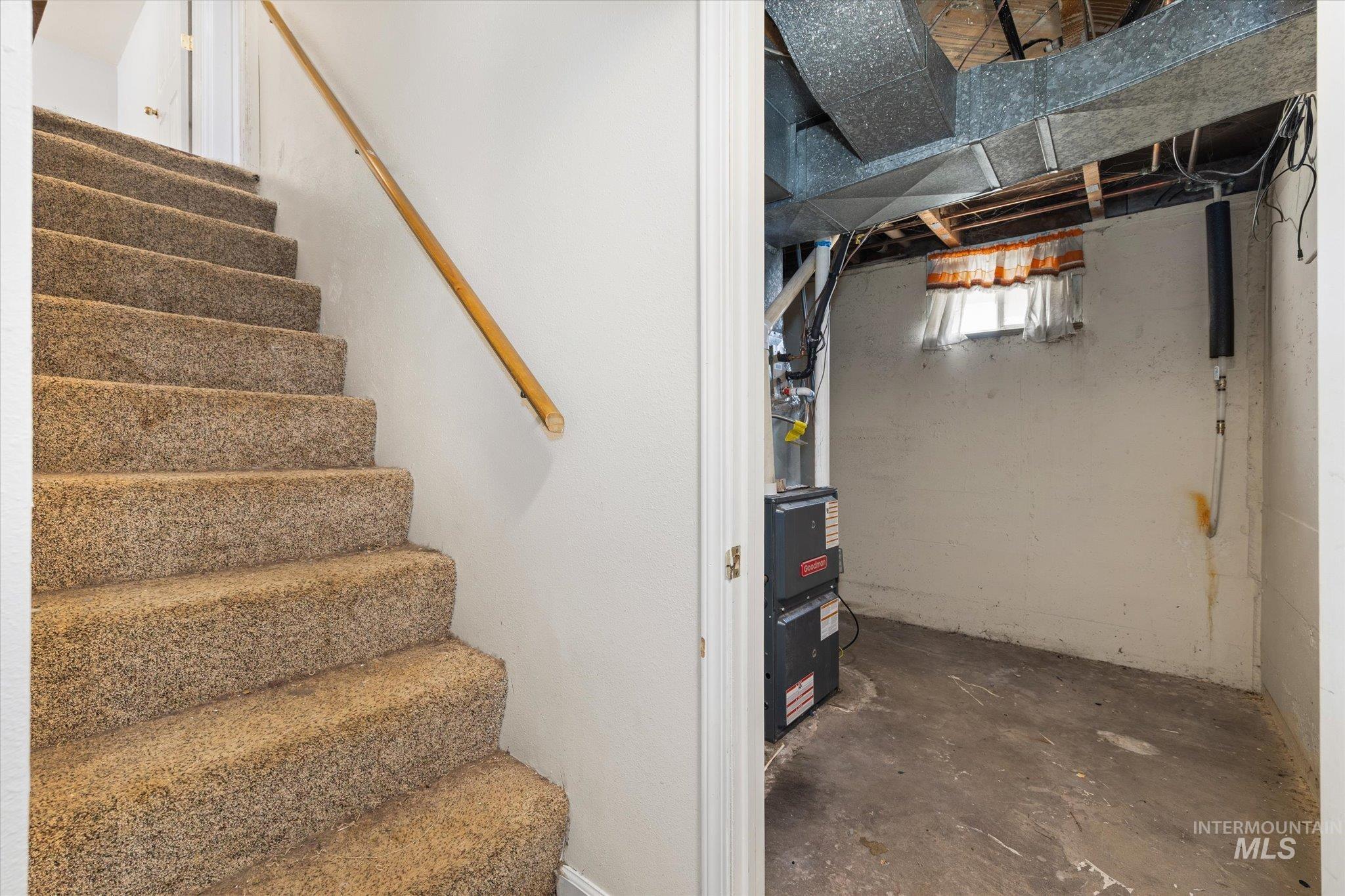 918 West 3rd Street Weiser, ID 83672 - Photo 30 of 36 Carpeted staircase with wood handrail, leading to a utility area featuring exposed ductwork, a furnace, and a small window