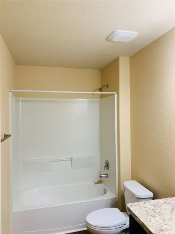 a bathroom with a granite countertop bathtub shower sink vanity and a toilet
