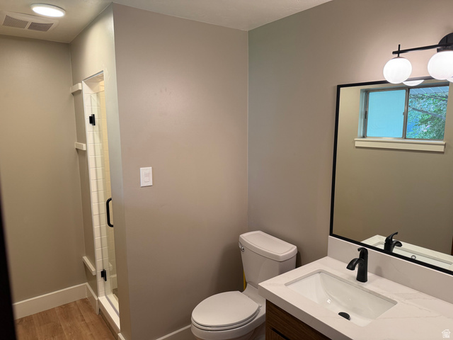 15 West 1600th Street South Mapleton, UT 84664 - Photo 7 of 22 Bathroom featuring a glass-enclosed shower, wood-finish flooring, a contemporary vanity with a white countertop, a rectangular undermount sink, and a black-framed mirror