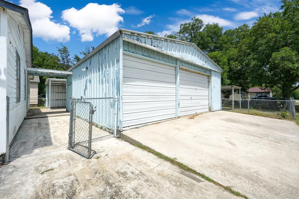 1802 Refinery Road Gainesville, TX 76240 - Photo 22 of 27 Two-bay garage with corrugated metal siding, featuring a concrete driveway and chain-link fencing
