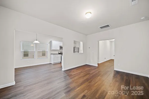 a view of empty room with wooden floor and kitchen