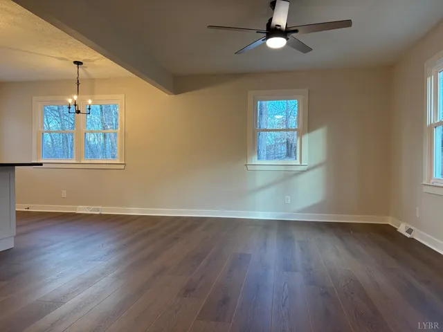 an empty room with wooden floor chandelier and windows
