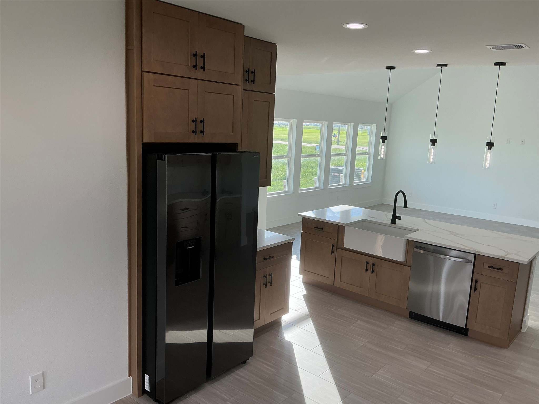 471 Buffalo Trail Angleton, TX 77515 - Photo 14 of 35 This modern kitchen features sleek black appliances, wooden cabinetry, and a spacious island with a farmhouse sink. The open layout is enhanced by large windows allowing natural light and contemporary pendant lighting.