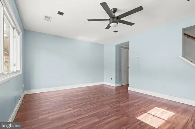 an empty room with wooden floor fan and windows