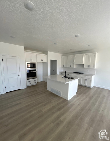 2720 West Aurora Avenue Mapleton, UT 84664 - Photo 4 of 11 Kitchen featuring white cabinets, a kitchen island with sink, stainless steel oven, light wood-type flooring, and a textured ceiling