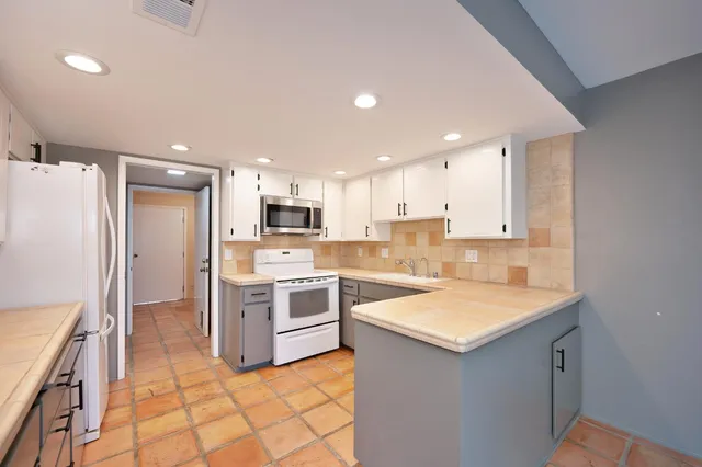 a kitchen with a sink a stove a refrigerator and a stove top oven with white cabinets