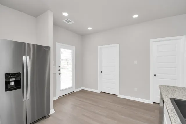 a view of an empty room with wooden floor and a kitchen