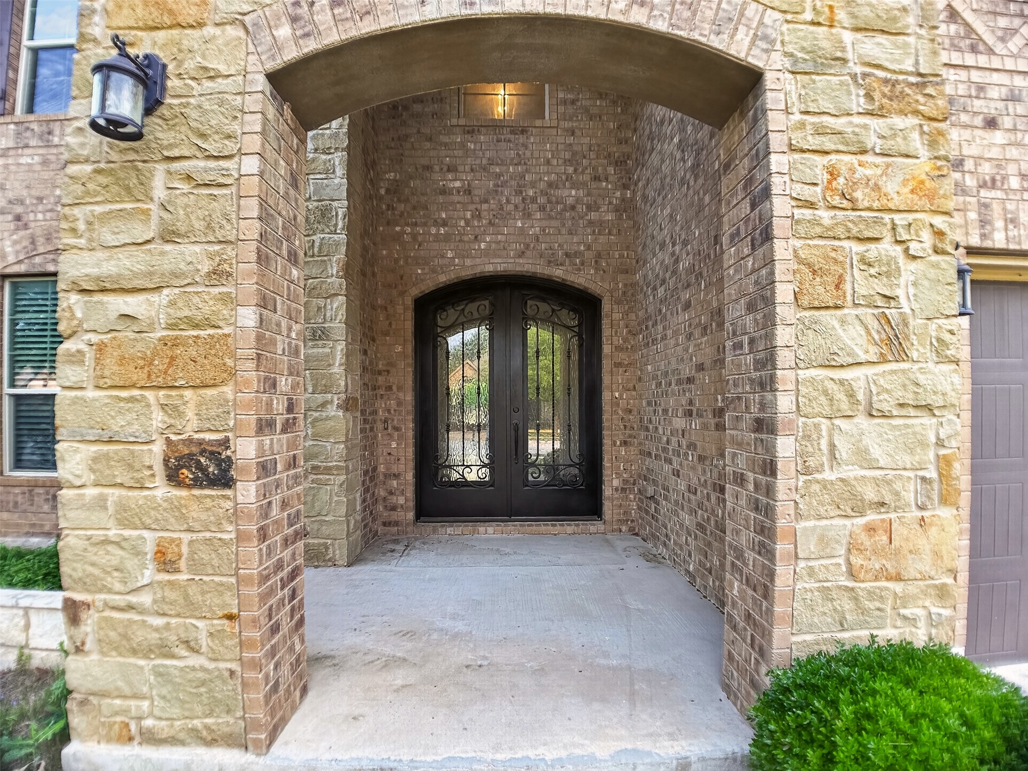 1505 Long Shadow Lane Georgetown, TX 78628 - Photo 2 of 28 Arched stone and brick entryway featuring double iron-accented glass doors and a wall-mounted exterior light fixture