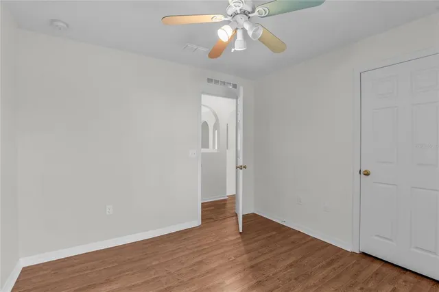 an empty room with wooden floor fan and windows