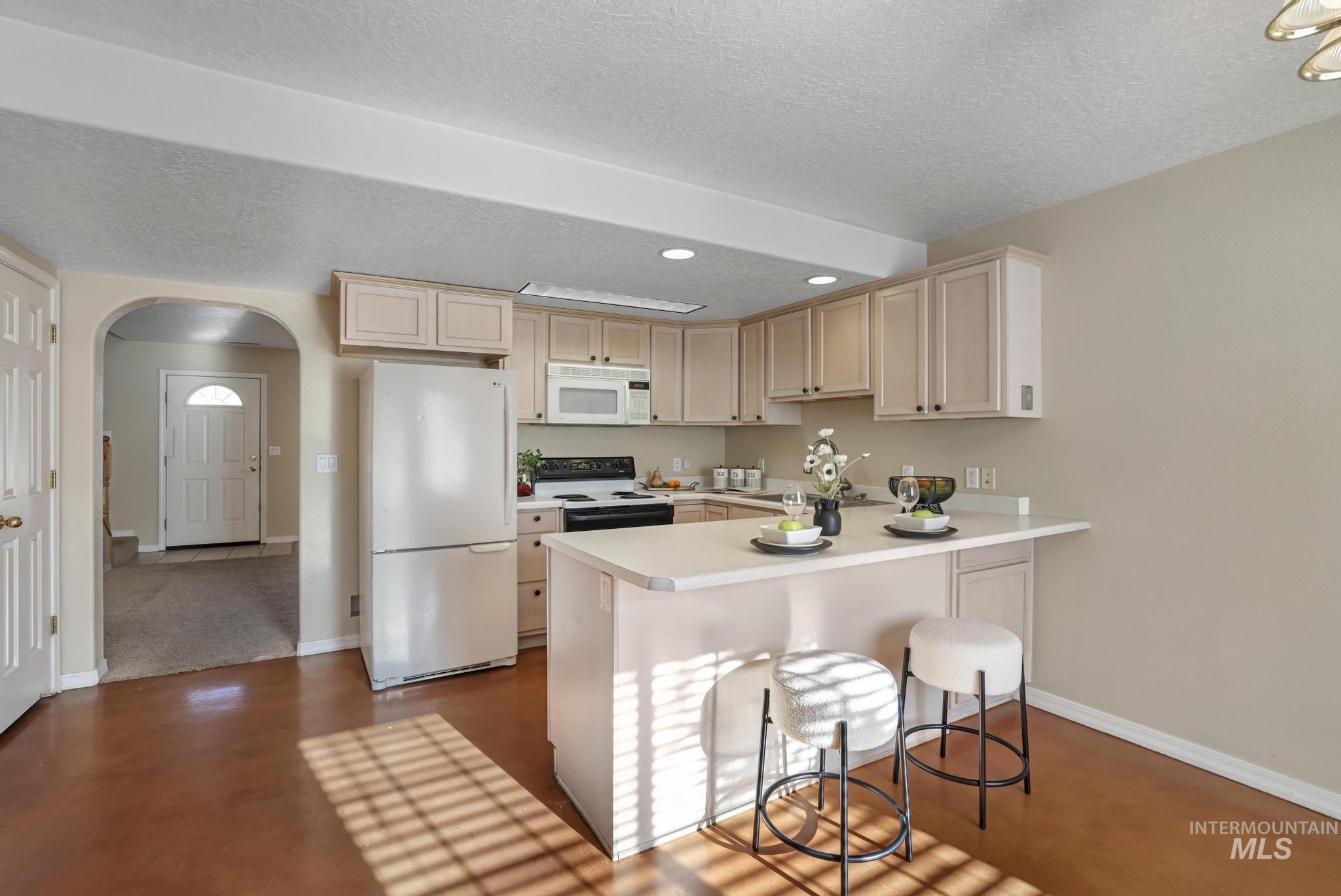1935 Hampton Way Twin Falls, ID 83301 - Photo 9 of 25 Kitchen featuring arched walkways, white appliances, light countertops, a breakfast bar, and a textured ceiling