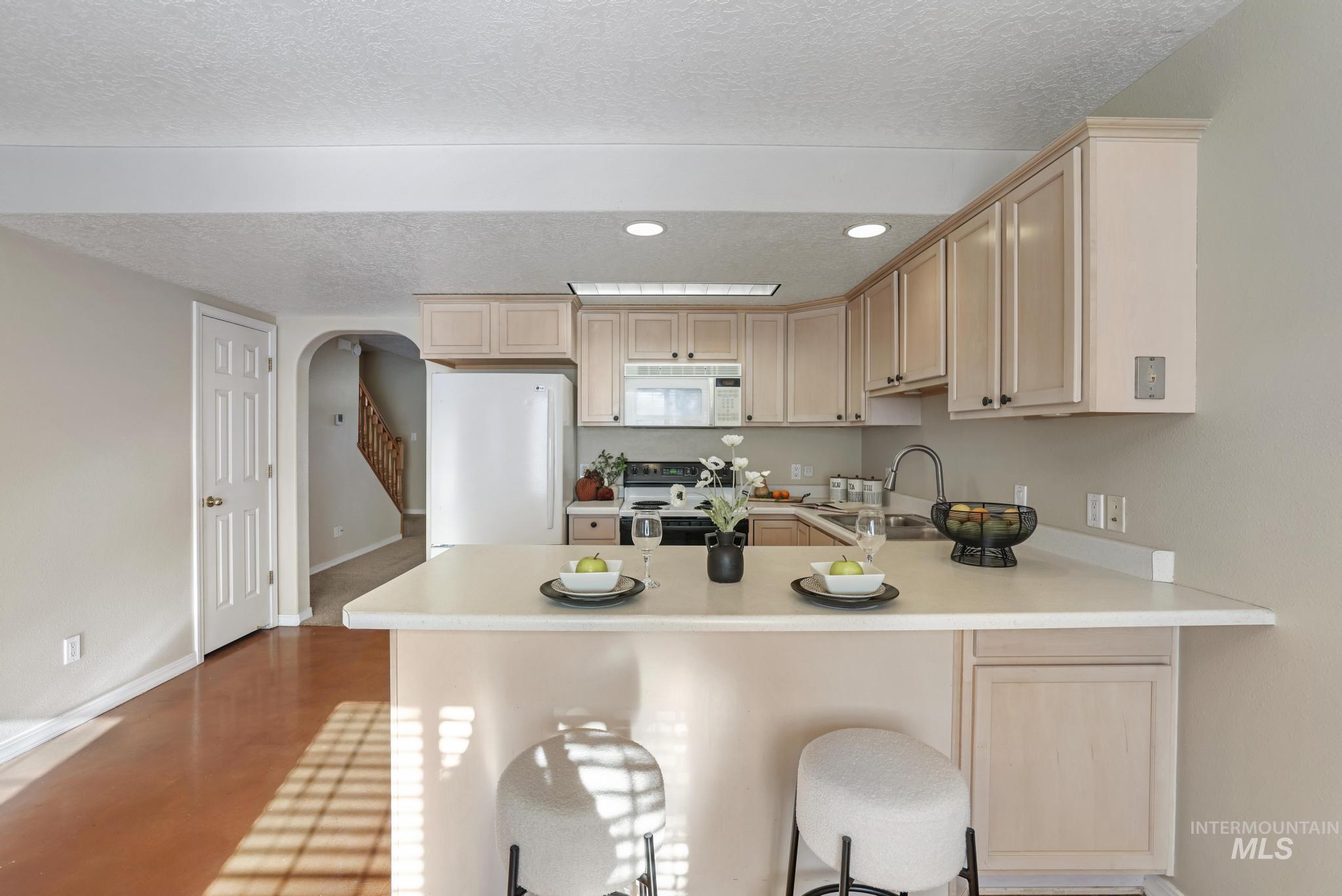 1935 Hampton Way Twin Falls, ID 83301 - Photo 10 of 25 Kitchen with a textured ceiling, a kitchen breakfast bar, white appliances, light brown cabinetry, and light countertops