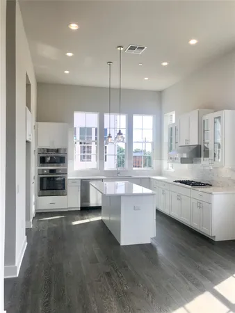 a large kitchen with kitchen island a stove a sink a refrigerator and white cabinets with wooden floor