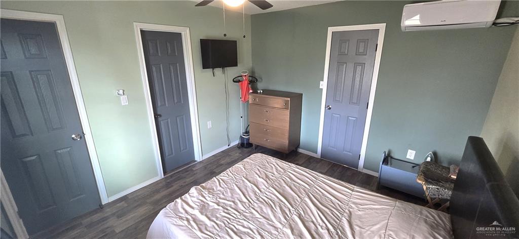 189 Midway Road Rio Grande City, TX 78582 - Photo 8 of 20 Room featuring wood-finish flooring, two paneled doors with white trim, a ceiling fan, and a wall-mounted air conditioning unit