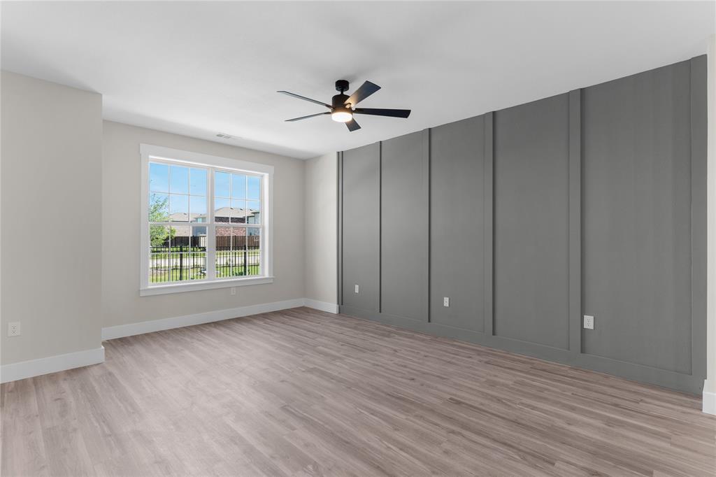 1650 Palladio Loop, Unit 2 Princeton, TX 75407 - Photo 3 of 14 Spacious room featuring wood-finish flooring, a contemporary ceiling fan with integrated lighting, and a prominent accent wall with vertical paneling