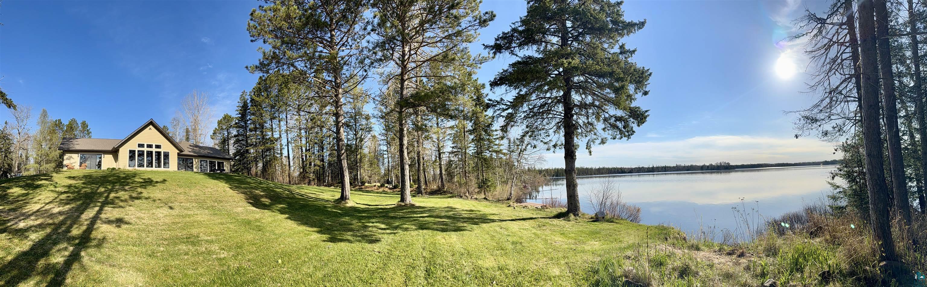 5274 Marble Lake Road Two Harbors, MN 55616 - Photo 2 of 79 Waterfront property featuring a sloped lawn leading to the water's edge, mature trees, and a house with a gabled roofline and large windows