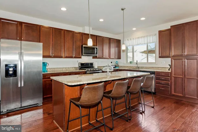 a kitchen with stainless steel appliances granite countertop a refrigerator a stove a sink a microwave and white cabinets with wooden floors