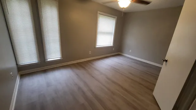 an empty room with wooden floor fan and window