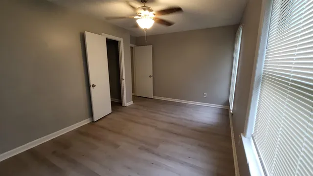 an empty room with wooden floor fan and windows