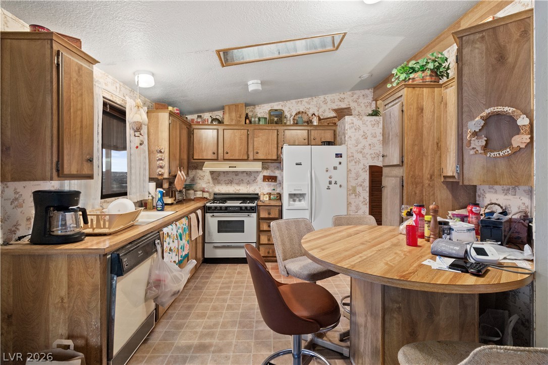 1609 Cajon Court Laughlin, NV 89029 - Photo 11 of 69 Kitchen with wallpapered walls, white appliances, a kitchen breakfast bar, wood finish cabinets, and a peninsula