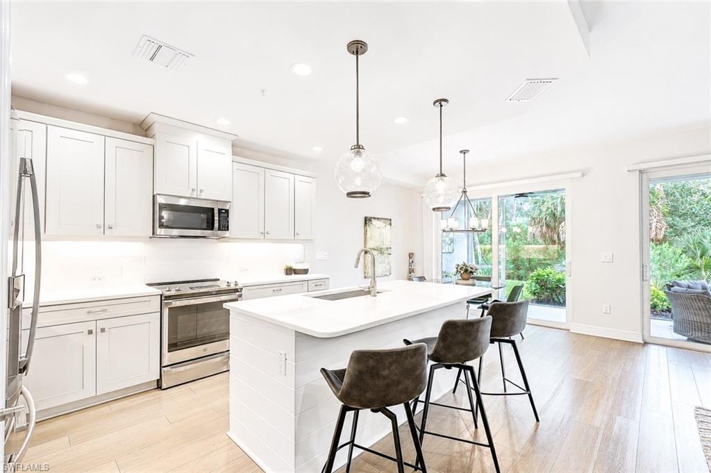 2620 Seychelles Circle, Unit 1302 Naples, FL 34112 - Photo 6 of 43 a kitchen with stainless steel appliances kitchen island a stove a sink a refrigerator a dining table and chairs with wooden floor