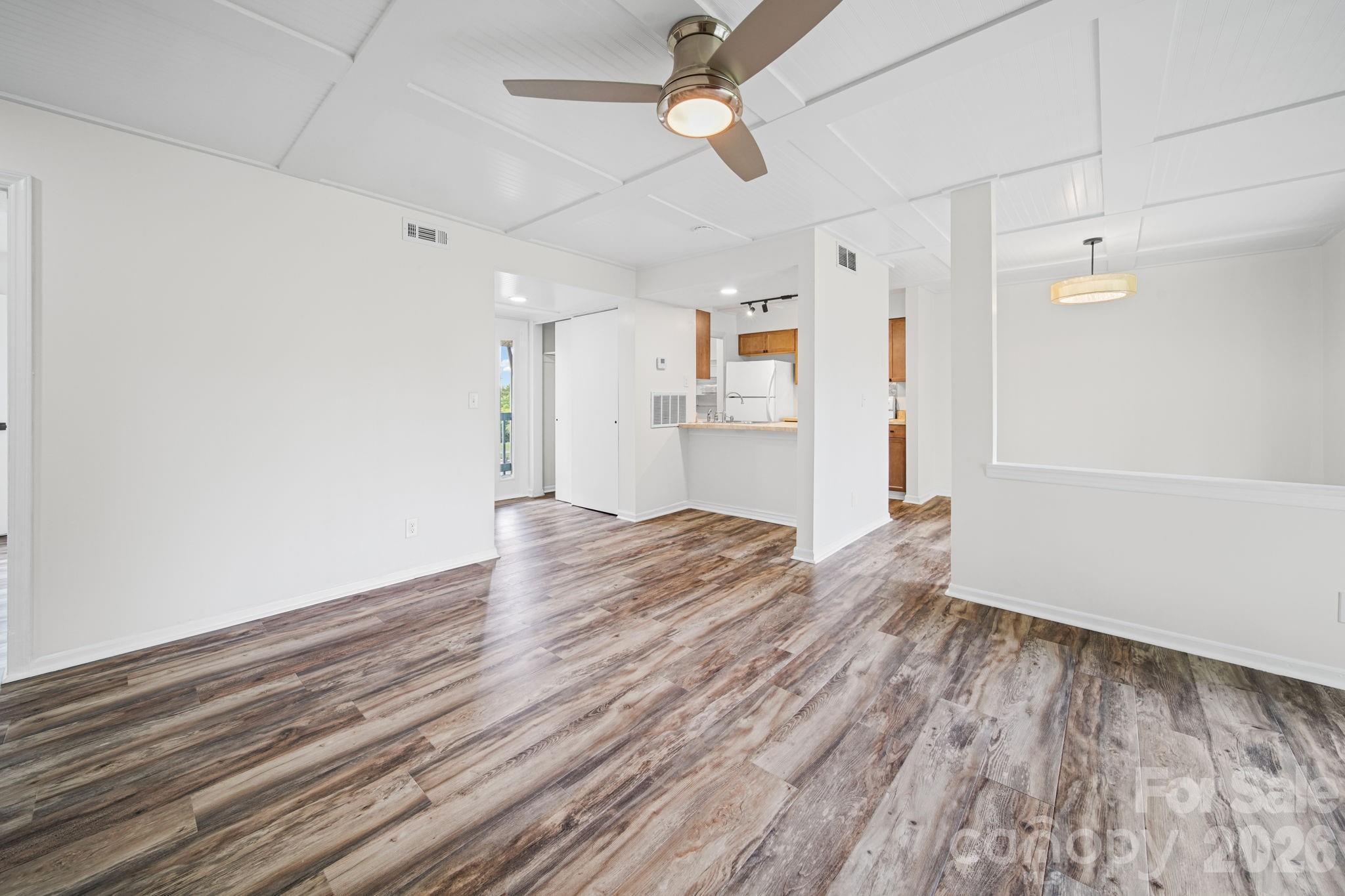 11023 Harrowfield Road Charlotte, NC 28226 - Photo 4 of 32 an empty room with wooden floor a ceiling fan and kitchen view