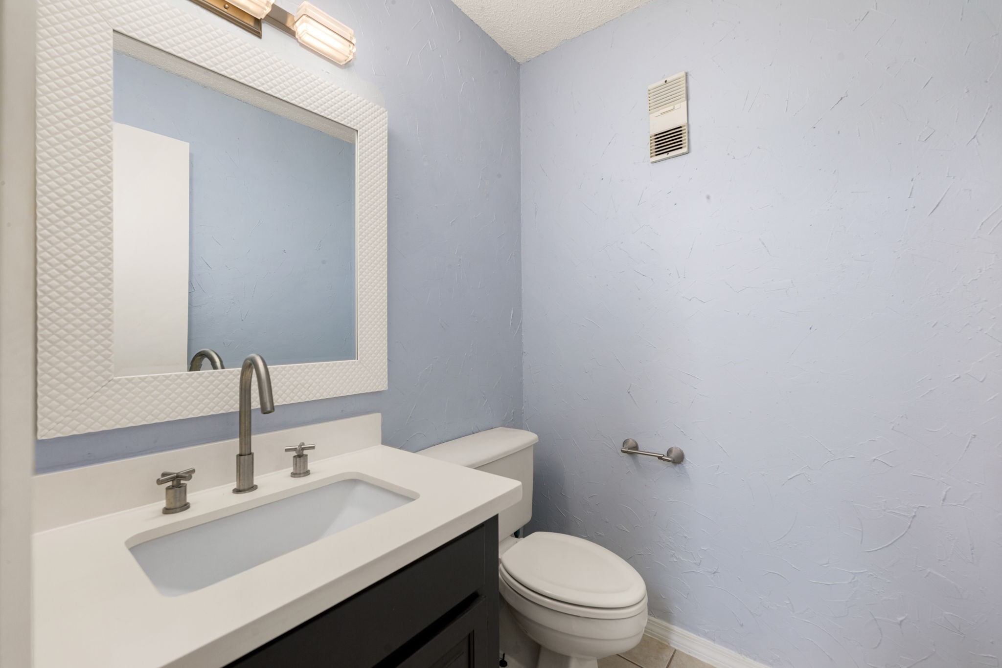 3200 South Gessner Road, Unit 228 Houston, TX 77063 - Photo 9 of 18 The conveniently located powder bath features a dark vanity with quartz countertop, undermount sink, modern brushed nickel fixtures, a stylish framed mirror, and a pop of color with a soft blue accent wall, a charming and functional space for guests!
