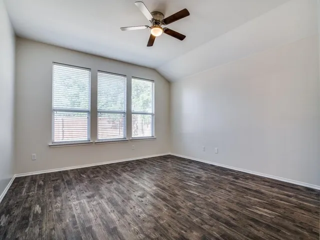 an empty room with wooden floor fan and windows