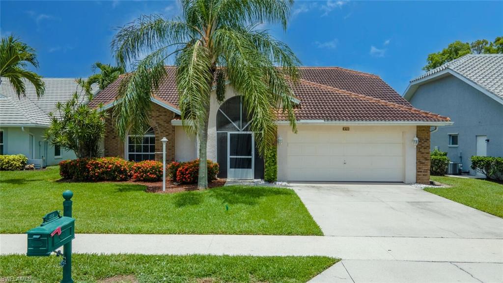 458 Countryside Drive Naples, FL 34104 - Photo 3 of 50 View of front facade with a front yard, a garage, concrete driveway, brick siding, and a tile roof