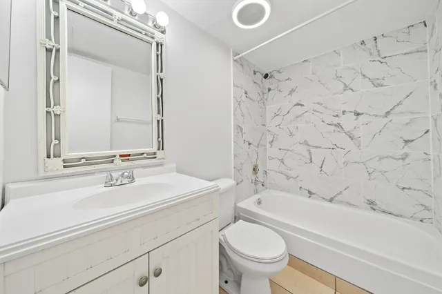 a bathroom with a granite countertop sink a toilet a mirror and bathtub