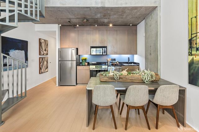 a kitchen with stainless steel appliances kitchen island granite countertop a dining table chairs and a refrigerator