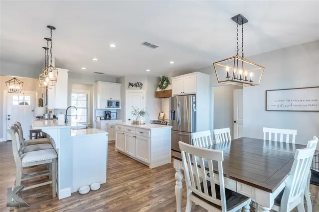 a kitchen with stainless steel appliances kitchen island granite countertop a dining table chairs and white cabinets