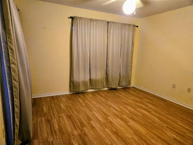 an empty room with wooden floor and windows with curtains