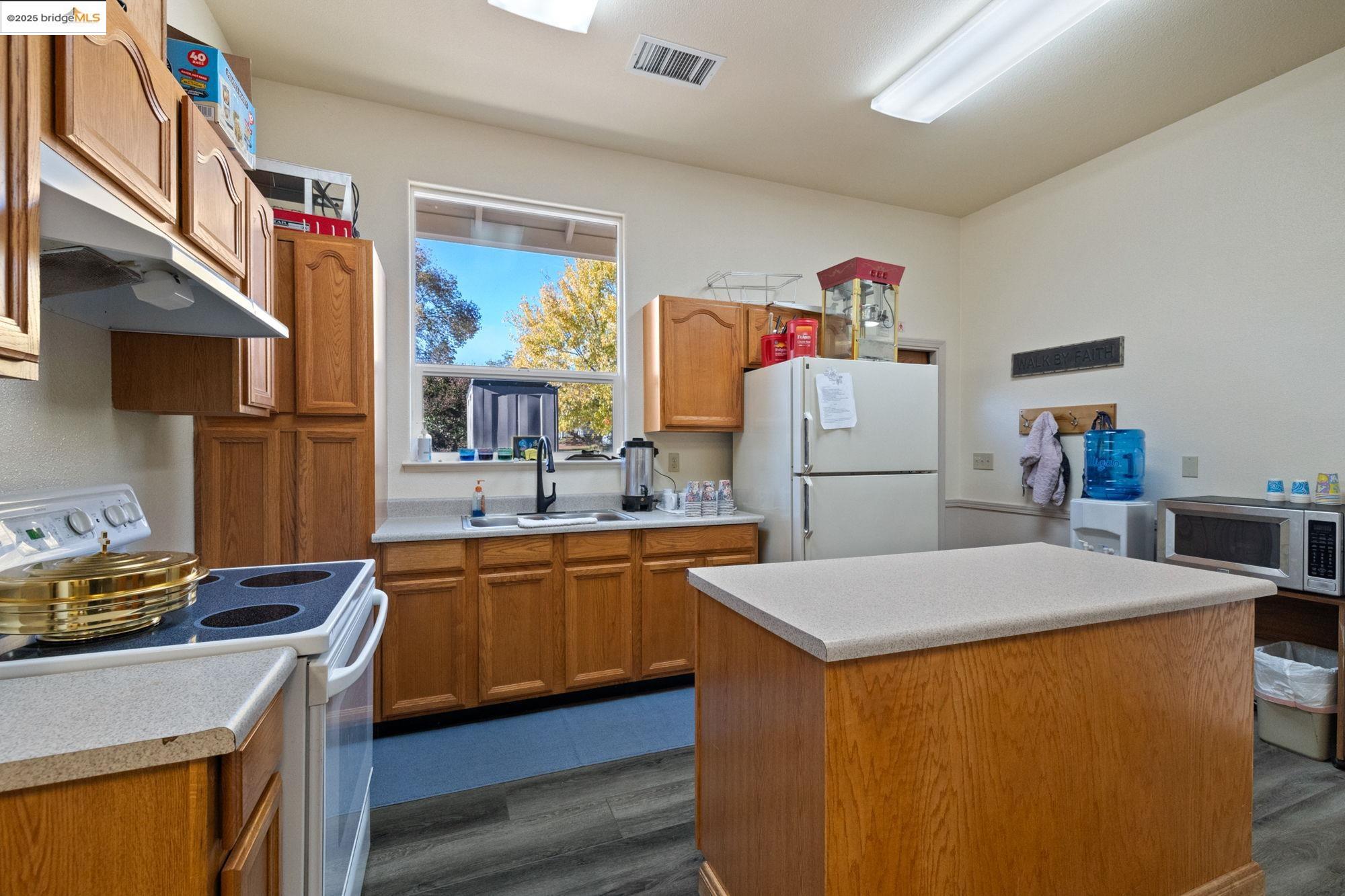 5033 Main Street Coulterville, CA 95311 - Photo 22 of 38 Kitchen featuring white appliances, light countertops, under cabinet range hood, brown cabinetry, and a center island