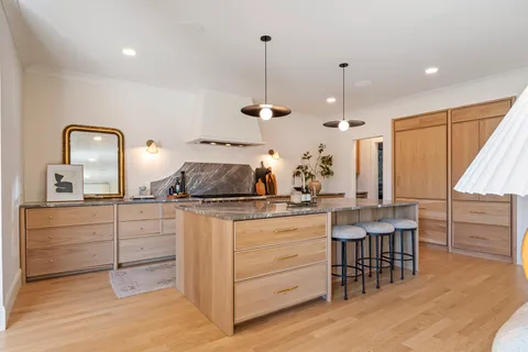 a kitchen with kitchen island granite countertop a stove a chimney a sink and cabinets