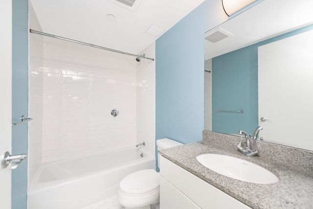 a bathroom with a granite countertop bathtub shower sink vanity mirror and toilet