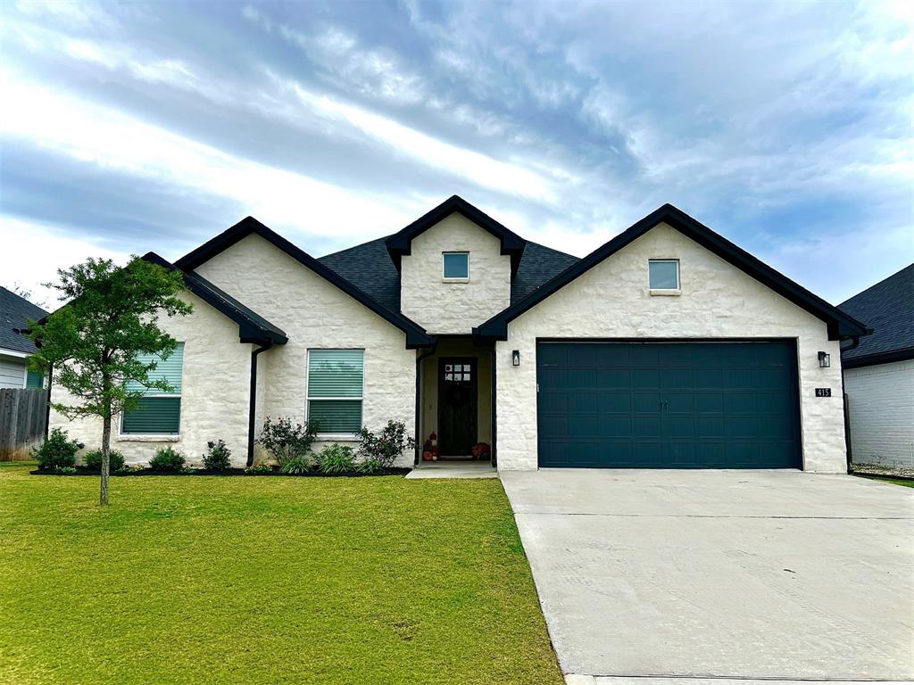 View of front of property featuring stone siding, concrete driveway, a front yard, and a garage